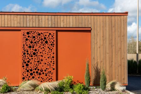 Moderne Fassade mit orangefarbenem Schiebeelement und Holzverkleidung.