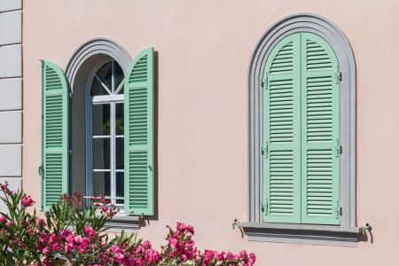 Bogenfenster mit hellgrünen Klappläden, links geöffnet, rechts geschlossen, an rosa Hauswand.