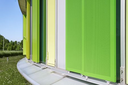 Detailansicht der Führungsschiene und Laufrollen von gelochten, grünen Aluminium-Schiebeläden an einer Glasfassade